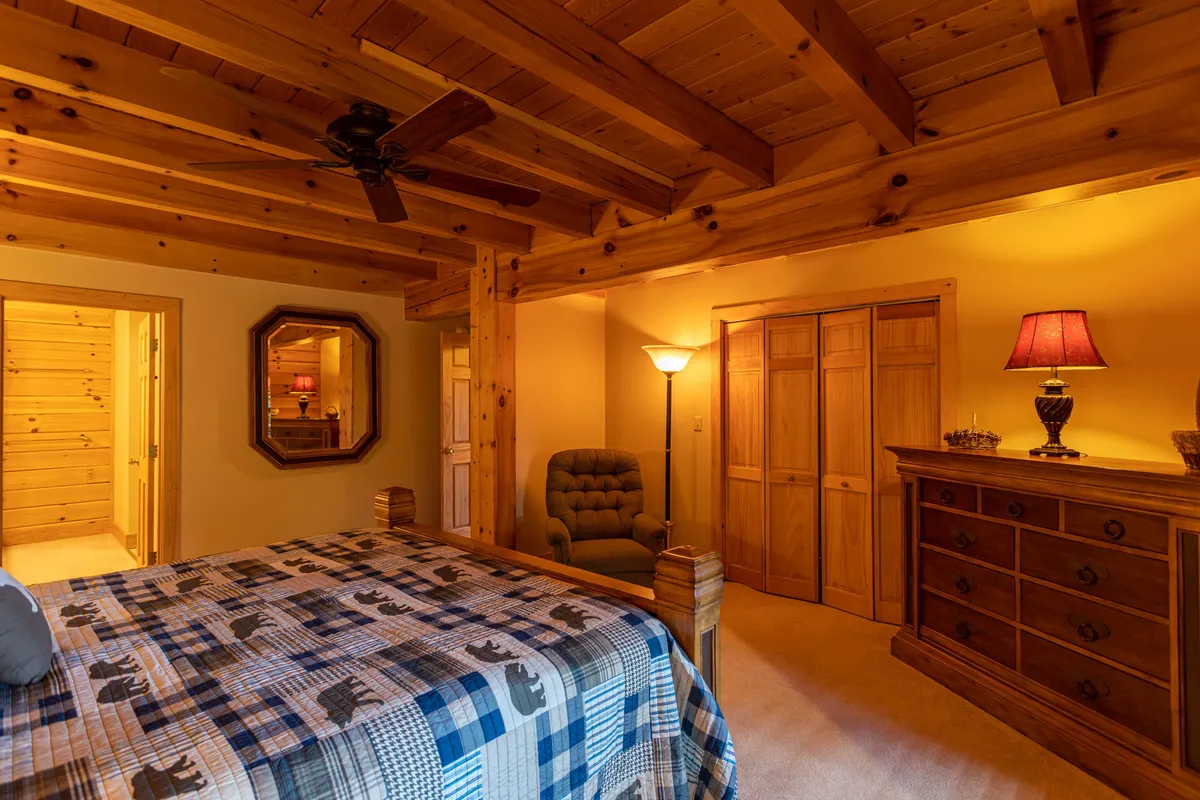 A cozy bedroom is shown with a patterned quilt on the bed, a wooden dresser, an armchair, and a mirror. The room feels intimate and inviting, offering a tranquil spot for rest and relaxation after a day of outdoor activity.
