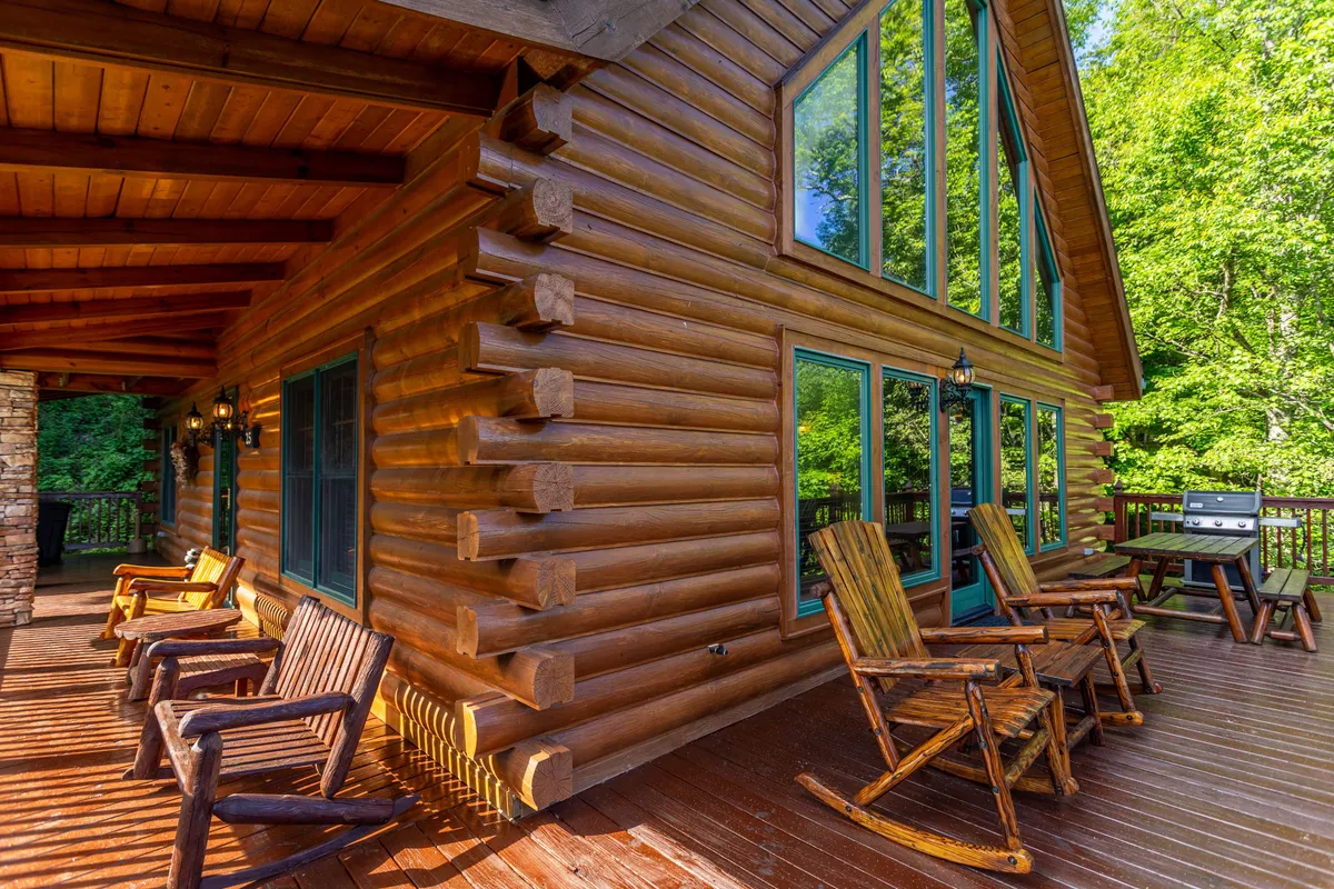 A welcoming log cabin exterior featuring large windows and a spacious deck with rocking chairs. The deck is surrounded by peaceful mountain scenery, making it an ideal spot for relaxing outdoors with pets. The log structure and inviting porch evoke a classic mountain retreat vibe.