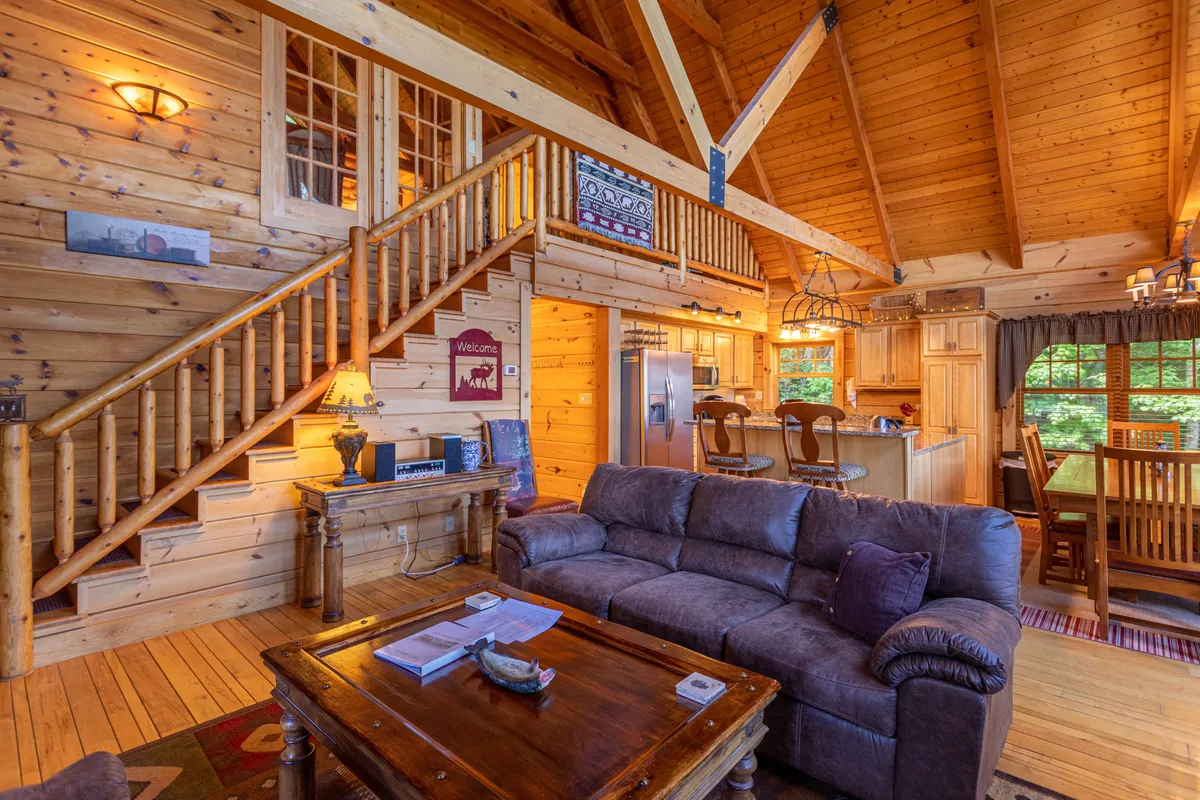 This interior shot emphasizes an open-concept layout with a comfortable sofa, a prominent staircase leading to additional levels, a modern kitchen area, and a spacious dining table. The space is designed for both relaxation and group meals, ideal for families or friends spending quality time together.