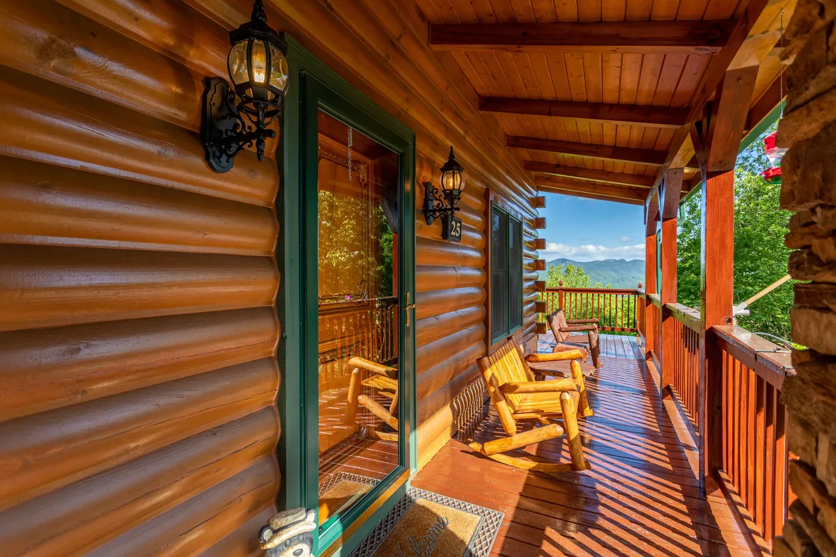 A charming exterior shot of the log cabin, featuring inviting wooden rocking chairs set on a spacious porch that looks out onto mountain vistas. Decorative lanterns and the natural wood structure create a welcoming alpine retreat vibe, while the mountain backdrop hints at the adventure beyond the doorstep.