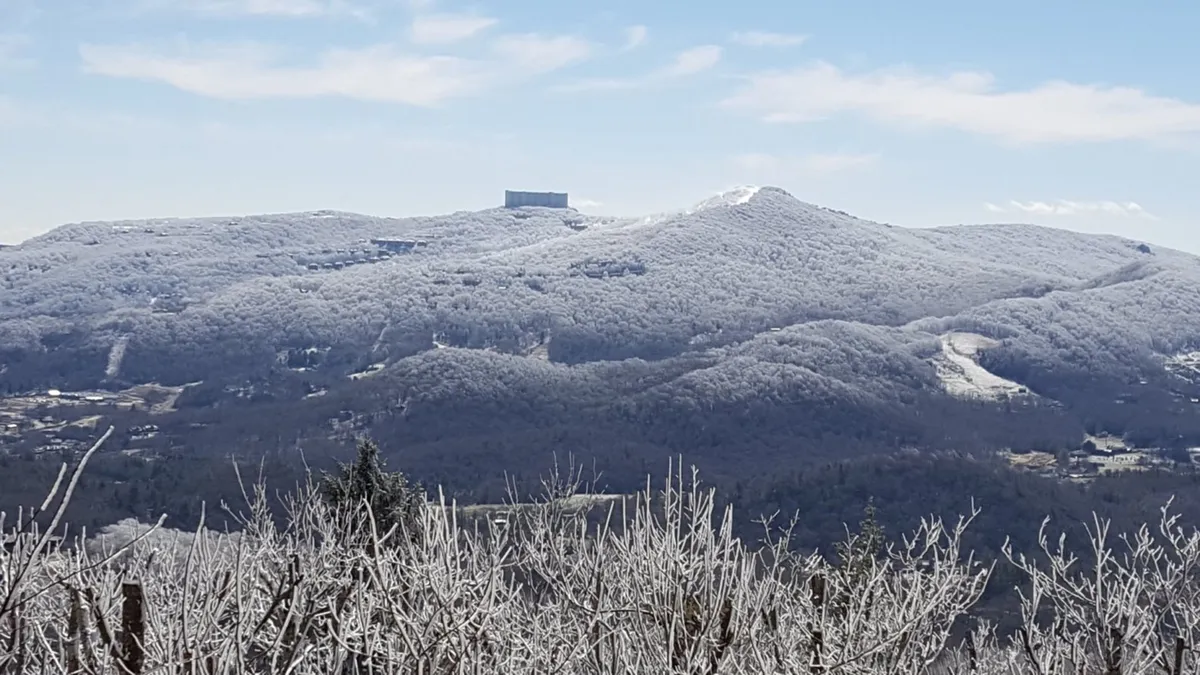 A stunning winter landscape scene with snow-covered mountains, frosted trees, and a distant building perched on a mountaintop. The serene and peaceful mood highlights the joys of winter activities like skiing and exploring snow-laden trails, evoking the thrill of nearby resorts.