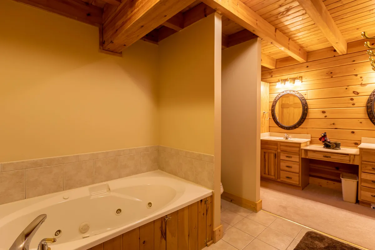 A luxurious bathroom featuring a spacious Jacuzzi tub, double vanity with round mirrors, and a wooden ceiling for rustic charm. Soft lighting enhances the space's tranquil and rejuvenating mood.