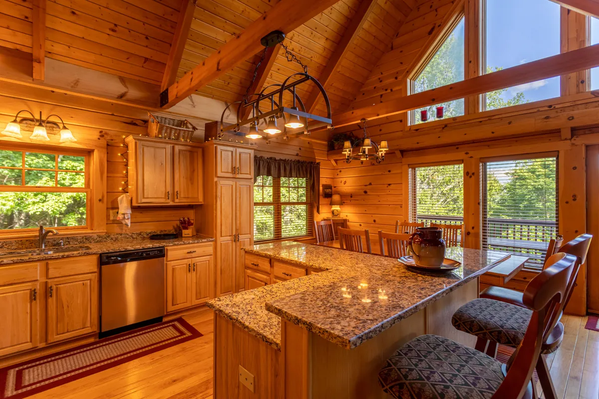 This image shows a kitchen with a granite countertop, large windows, wooden cabinets, and elegant chandeliers. The space feels welcoming and functional, encouraging group cooking, family gatherings, and festive celebrations. There's a sense of both style and practicality in the well-equipped setting.